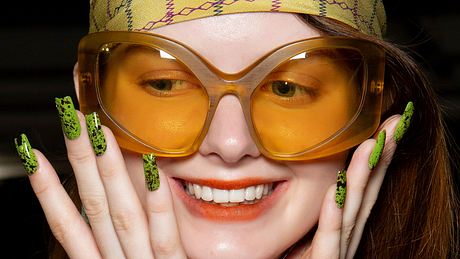Frau mit einer großen Sonnenbrille und einer grünen Maniküre grinst - Foto: Launchmetrics Spotlight