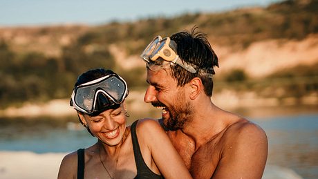 Frau und Mann flirten am Strand in Badeklamotten - Foto: iStock / Studio4