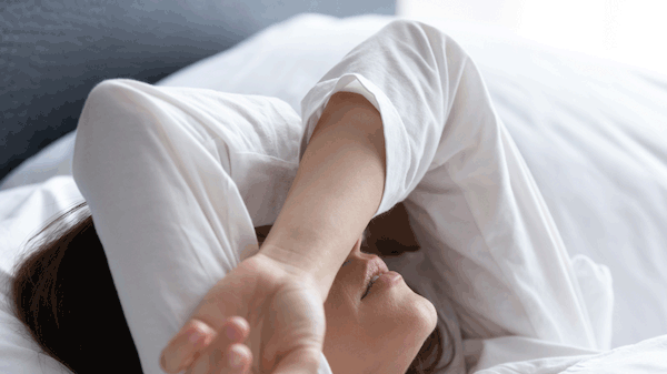 Frau liegt im Bett und verschränkt die Arme vor dem Gesicht - Foto: iStock / fizkes