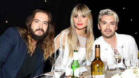 Tom Kaulitz, Heidi Klum und Bill Kaulitz sitzen an einem Tisch mit Bier, Wein und Wasser darauf - Foto: Getty Images / Tasia Wells 